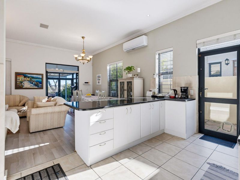 Open-plan kitchen and living area featuring white cabinetry, granite countertops, split-system air conditioning, and a seamless transition to the outdoor patio.