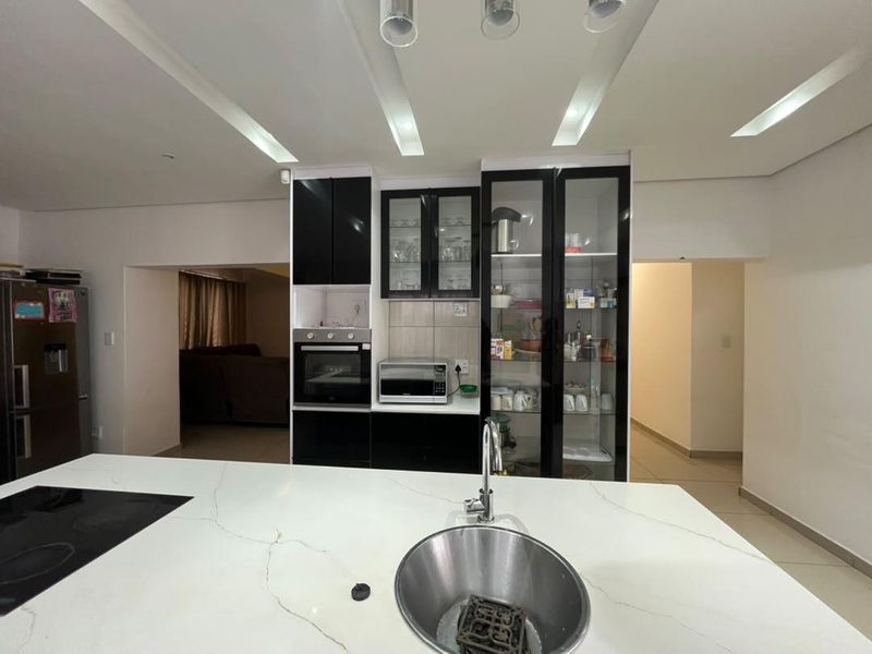 Modern kitchen featuring a central island with stone countertop, built-in oven, and sleek black cabinetry with glass-front display units.