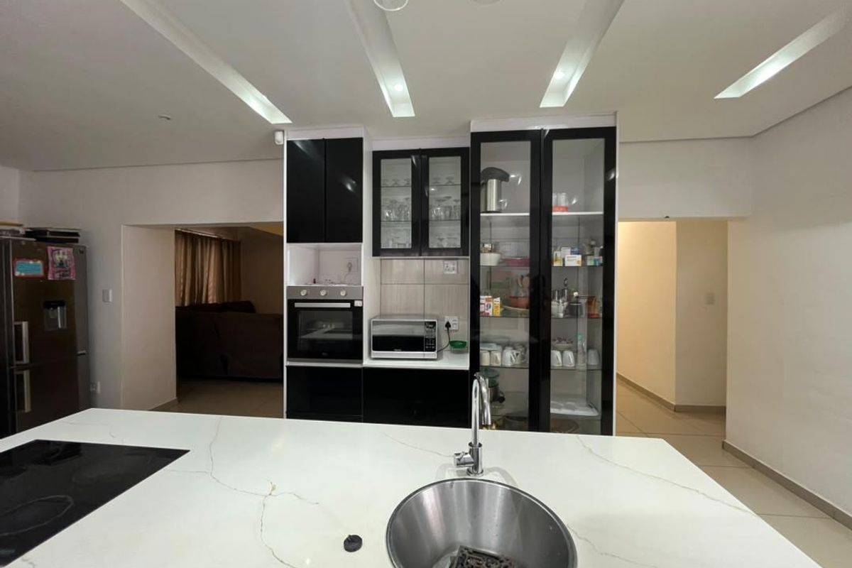 Modern kitchen featuring a central island with stone countertop, built-in oven, and sleek black cabinetry with glass-front display units.