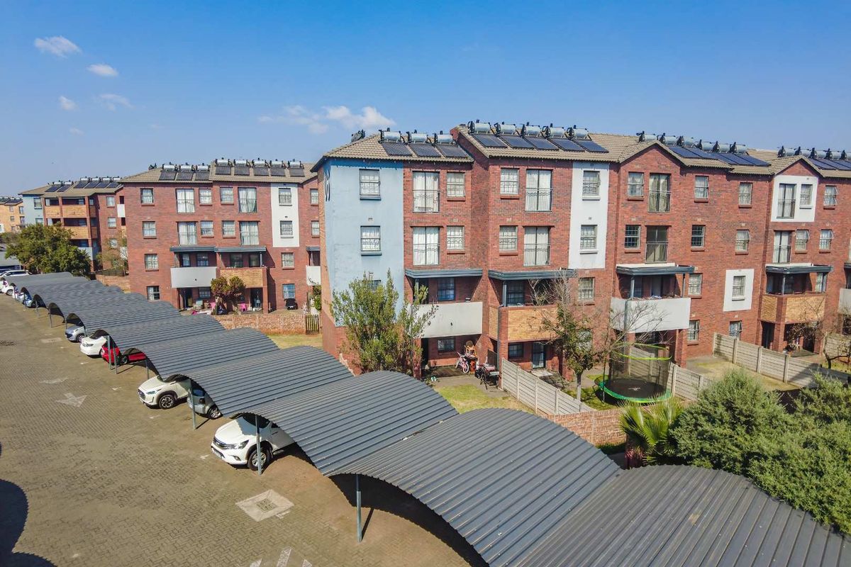 Aerial view of a multi-story brick apartment complex featuring covered parking bays, solar geysers, and landscaped ground-level areas.