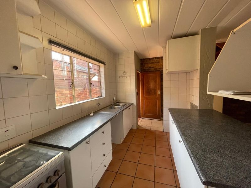 A dated kitchen featuring tiled splashbacks, laminate countertops, and a double basin sink, offering a functional layout ready for modernization.