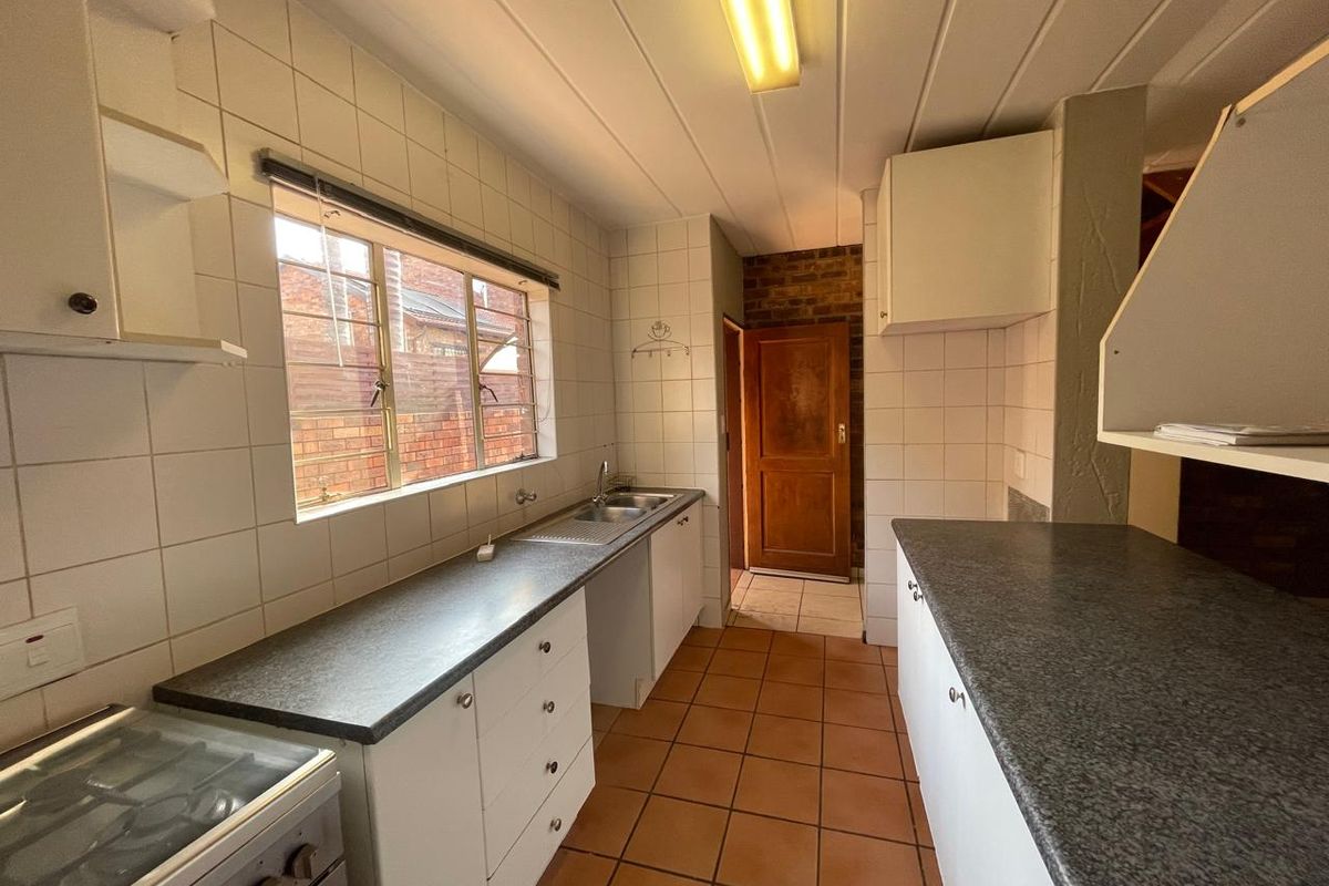 A dated kitchen featuring tiled splashbacks, laminate countertops, and a double basin sink, offering a functional layout ready for modernization.