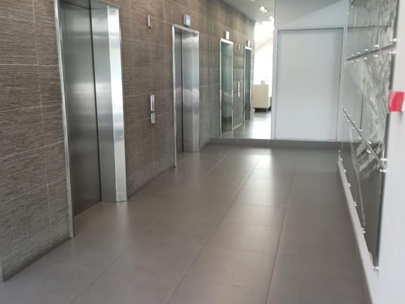 Modern office building elevator lobby featuring stainless steel lift doors, large wall mirrors, and contemporary tiled flooring with recessed lighting.