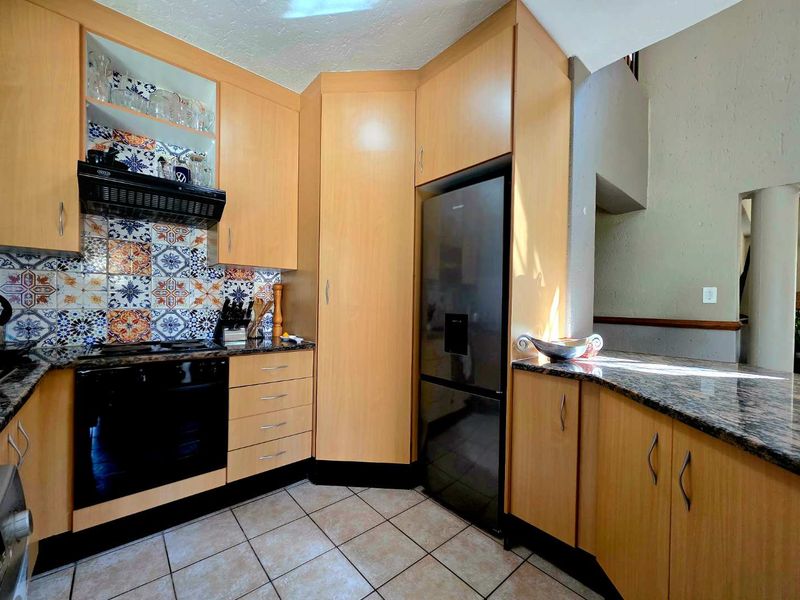 A functional kitchen featuring light wood cabinetry, granite countertops, a built-in oven, and decorative patterned tile backsplash.