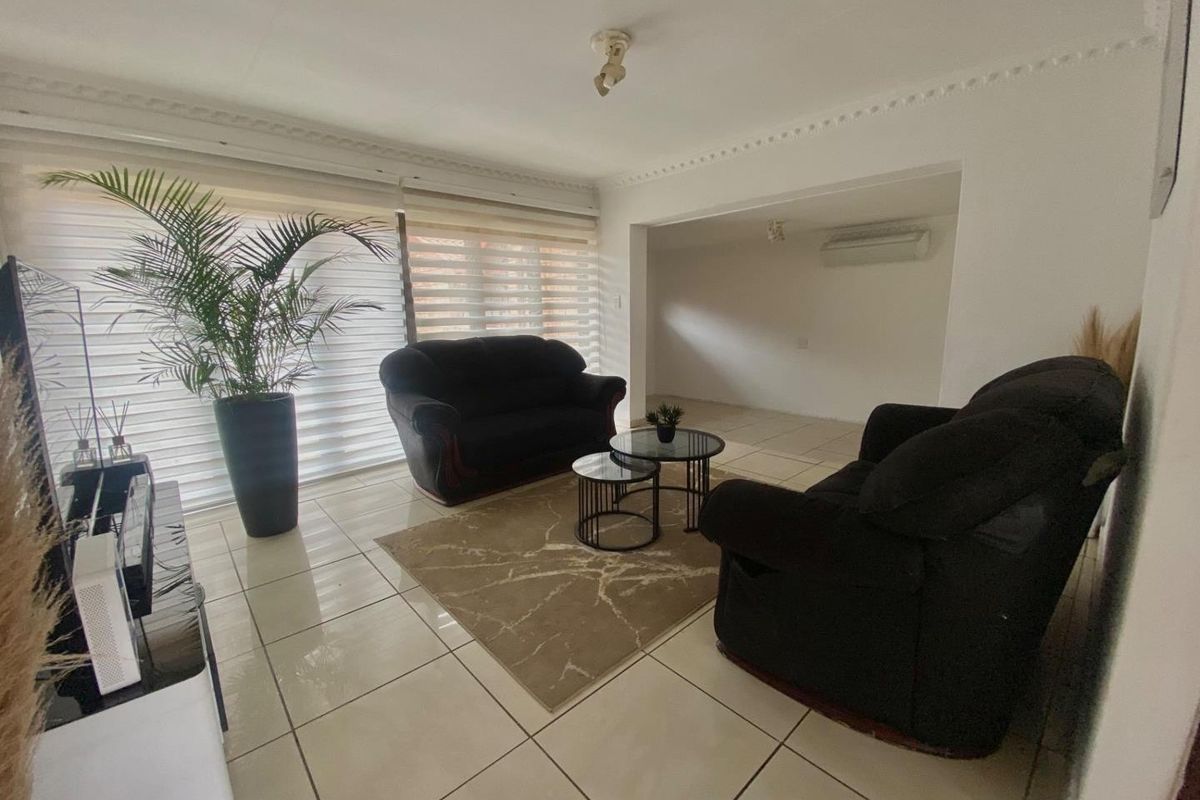 A spacious living area featuring tiled flooring, decorative ceiling cornices, and a wall-mounted air conditioning unit.