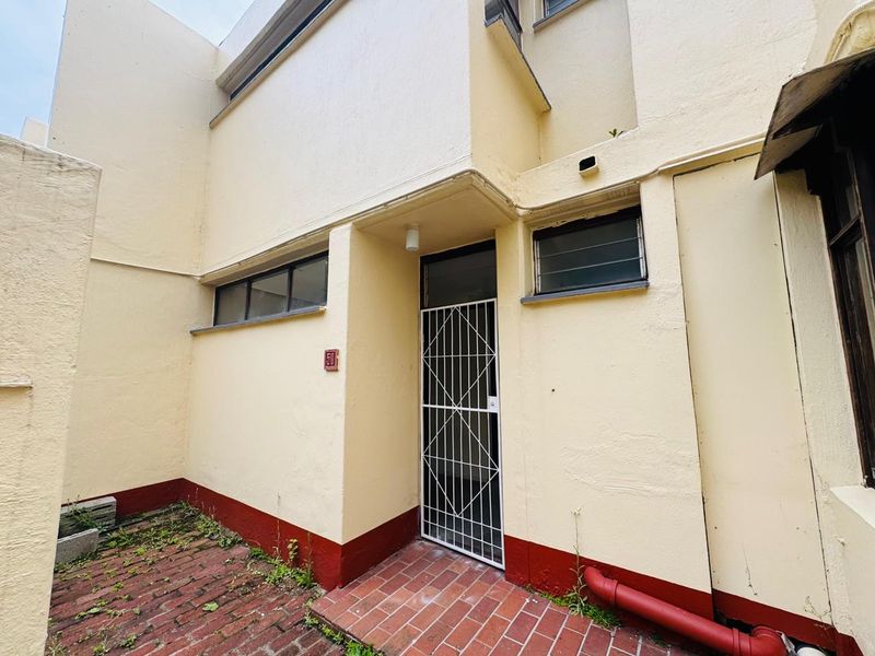 Front entrance of the apartment featuring a security gate, brick paved walkway, and exterior wall finishes requiring maintenance.
