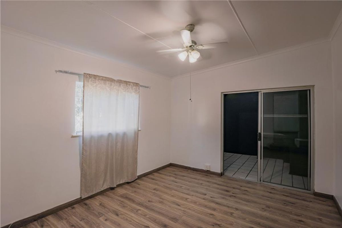 A bright, empty bedroom featuring wood-look laminate flooring, a ceiling fan, and sliding glass doors leading to an outdoor area.