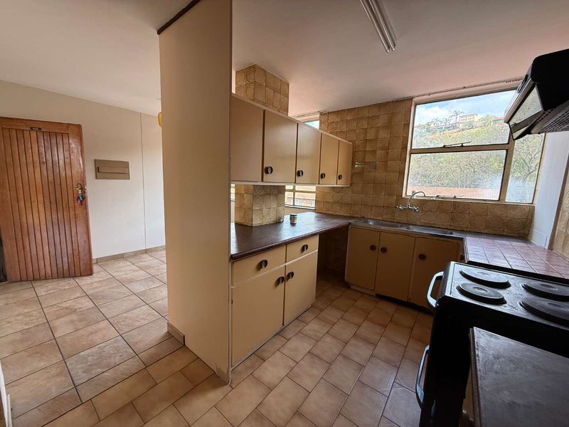 A functional kitchen featuring dated cabinetry, tiled backsplash, and tiled flooring, offering a blank canvas for modern renovation and design updates.