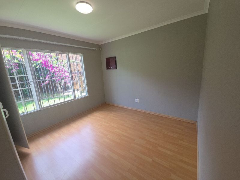A bright, empty bedroom featuring laminate flooring, neutral walls, and large windows fitted with security bars, offering a clean canvas for personalization.