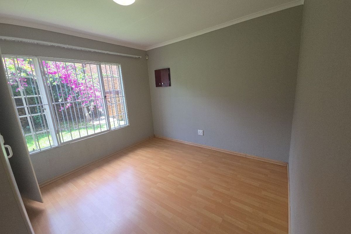 A bright, empty bedroom featuring laminate flooring, neutral walls, and large windows fitted with security bars, offering a clean canvas for personalization.