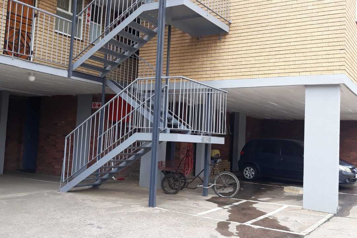 Exterior view of an apartment building featuring a metal staircase, brick facade, and covered parking area.