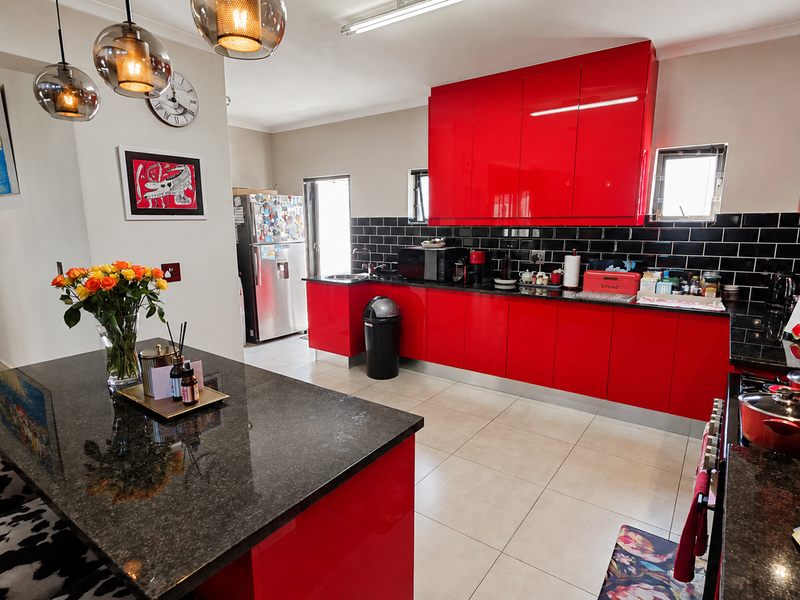Modern kitchen featuring high-gloss red cabinetry, black granite countertops, a central island, and a striking black subway tile backsplash with tiled flooring.