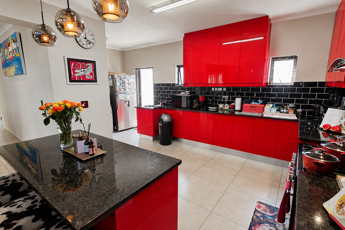 Modern kitchen featuring high-gloss red cabinetry, black granite countertops, a central island, and a striking black subway tile backsplash with tiled flooring.