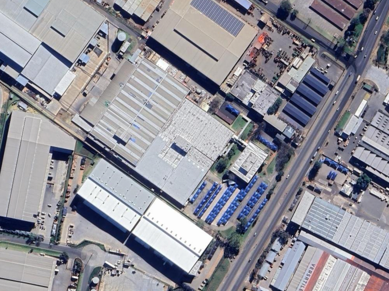 Aerial view of a large industrial complex featuring multiple warehouse structures, expansive roofing, and paved yard areas within an established industrial park.