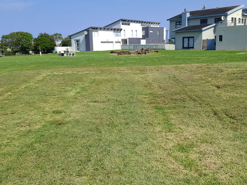 A view of a vacant residential plot featuring a well-maintained lawn and boundary wall, situated in a developed neighborhood.