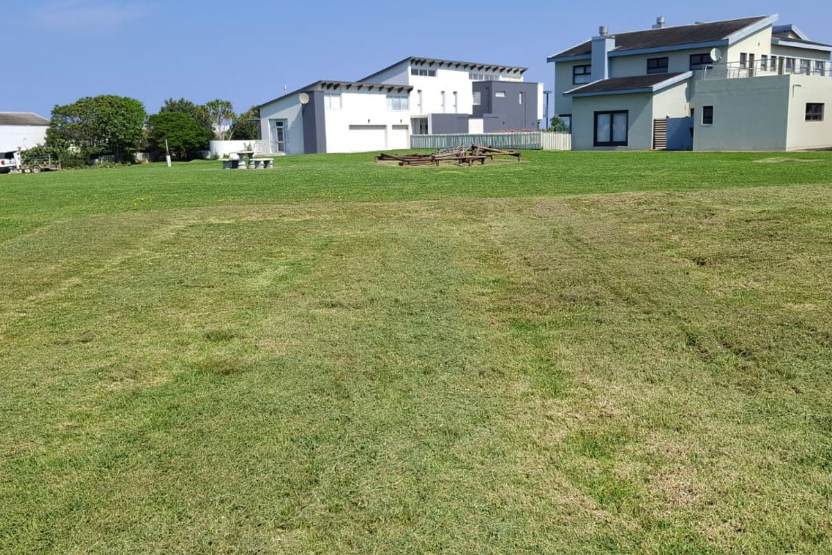 A view of a vacant residential plot featuring a well-maintained lawn and boundary wall, situated in a developed neighborhood.