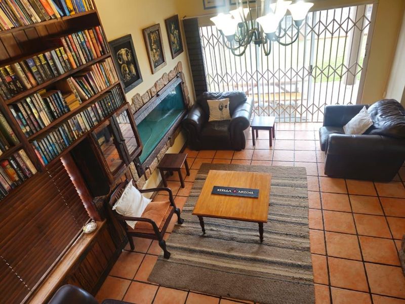 A living room featuring terracotta floor tiles, a built-in wooden bookshelf, a stone-clad feature wall, and access to the outdoors via a sliding security gate.