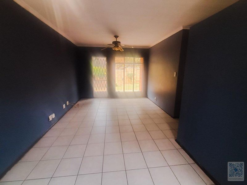 An empty living room featuring tiled flooring, a ceiling fan, and security bars on the windows and door.