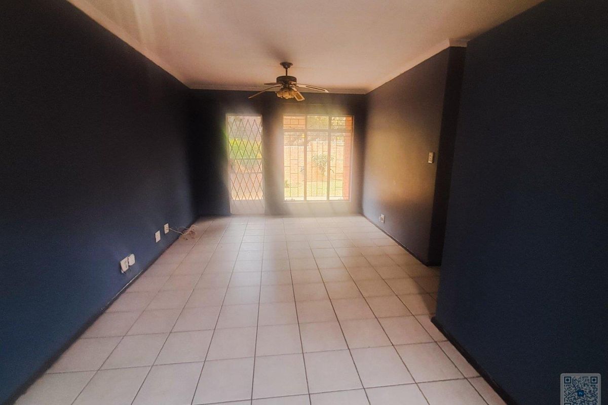 An empty living room featuring tiled flooring, a ceiling fan, and security bars on the windows and door.