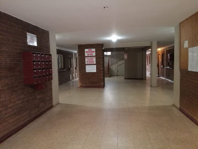 A communal apartment building hallway featuring brick walls, tiled flooring, a staircase, and a bank of mailboxes.