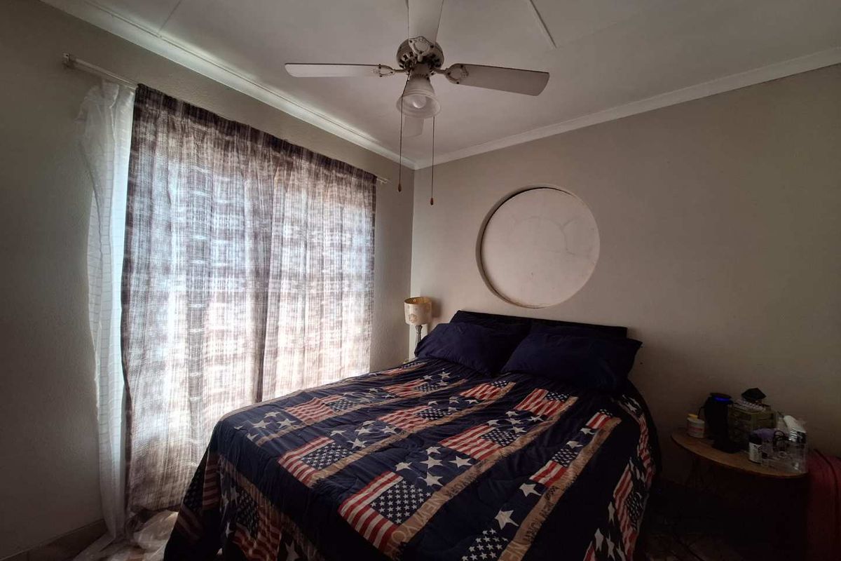A bedroom featuring a unique circular wall cutout, a ceiling fan, and tiled flooring, offering a functional space with potential for cosmetic updates.