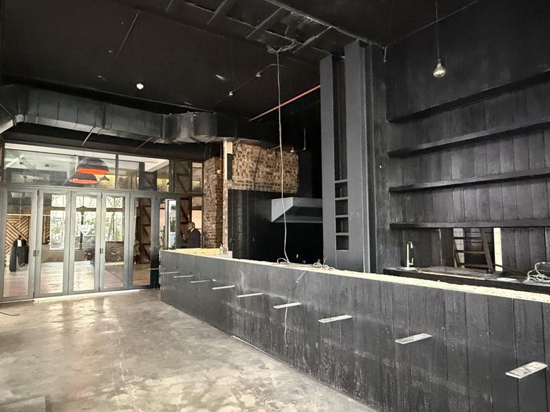 An industrial-style bar area featuring a large built-in counter, shelving, exposed ductwork, and glass folding doors, currently in an unfinished state.