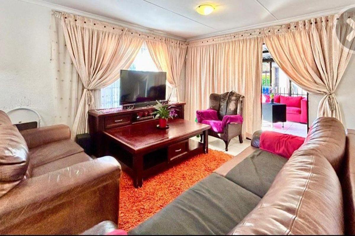 A comfortable living room featuring neutral walls, ceiling coving, and large windows dressed with curtains, providing a warm and inviting space for relaxation.