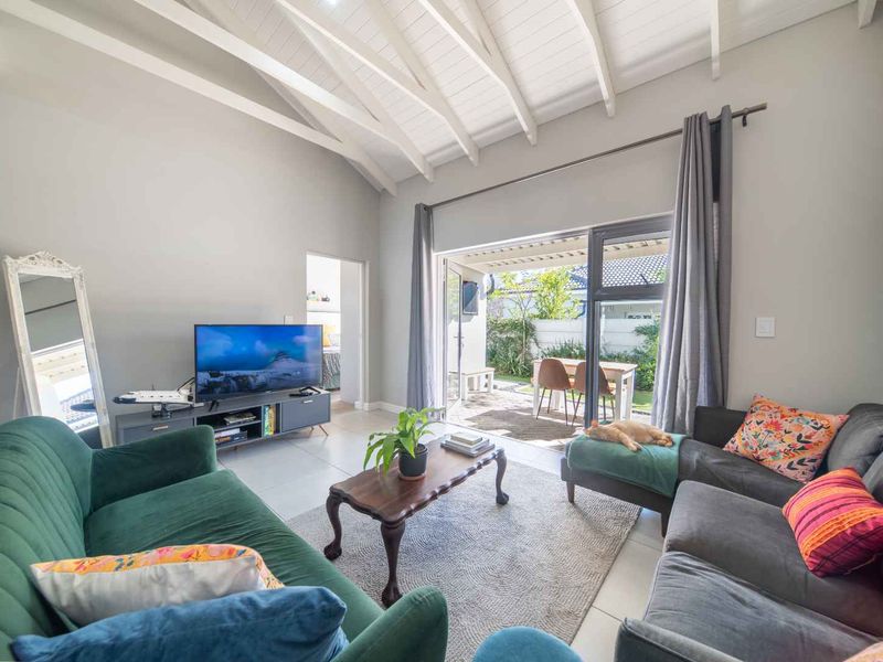 Bright living room featuring a high vaulted ceiling with exposed rafters, tiled floors, and large sliding doors opening onto a private patio area.