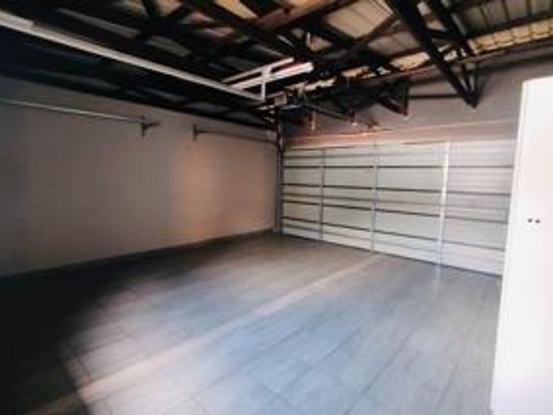A clean, spacious double garage featuring tiled flooring, exposed roof trusses, and a modern sectional garage door.
