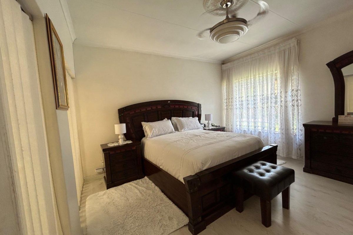 A well-maintained bedroom featuring light-toned laminate flooring, a decorative ceiling rose, and a ceiling fan.