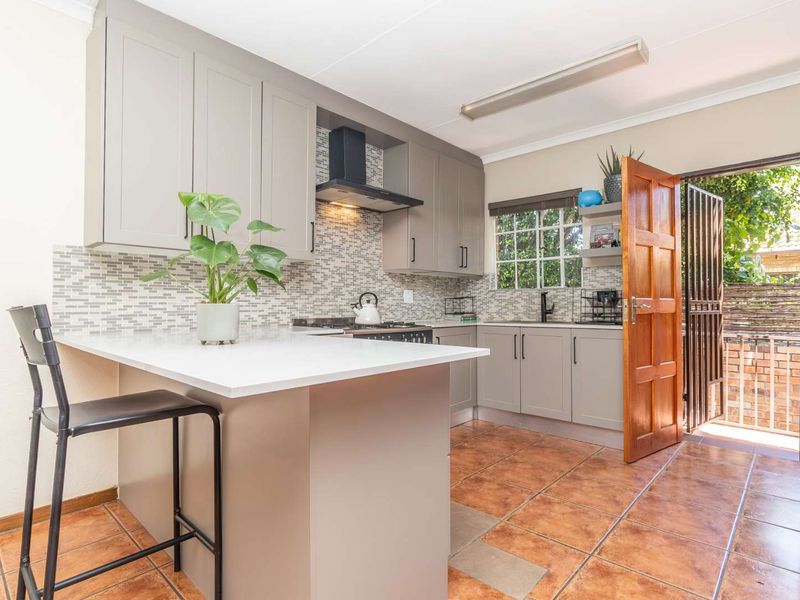 Modern kitchen featuring grey cabinetry, stone countertops, mosaic backsplash, and direct access to an outdoor area through a wooden door.