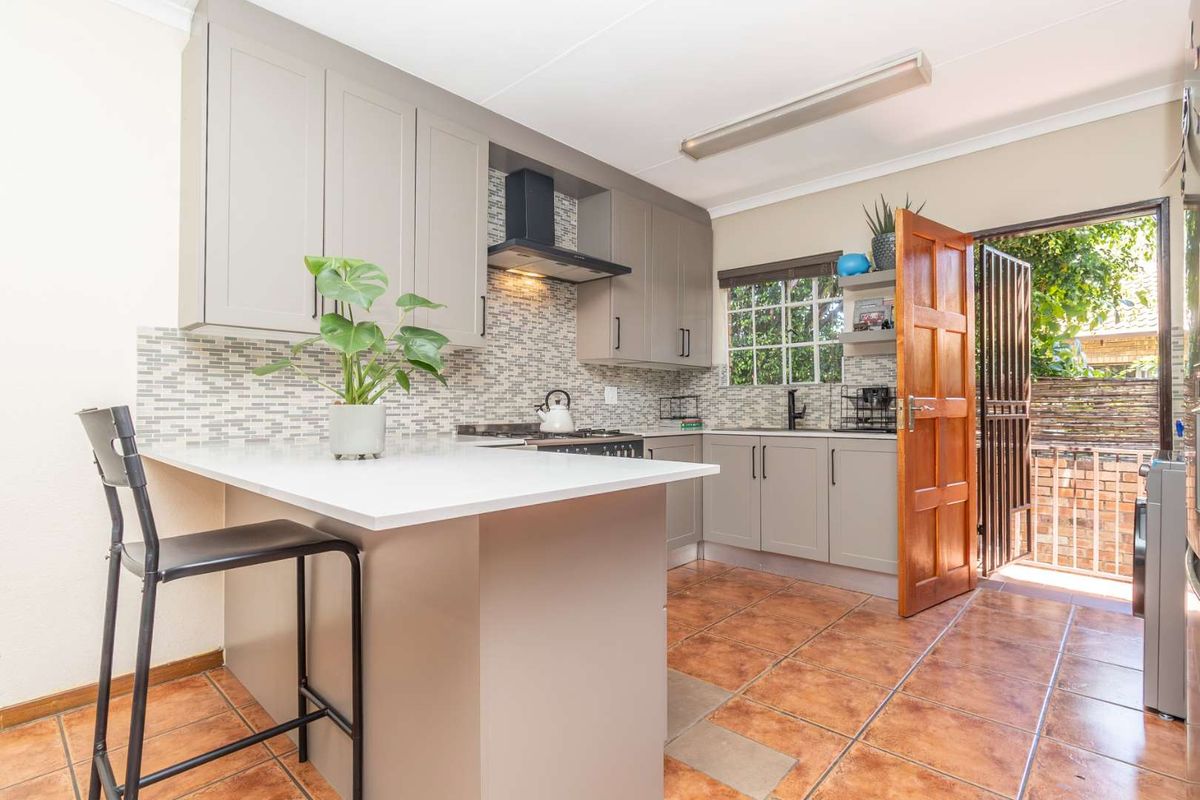 Modern kitchen featuring grey cabinetry, stone countertops, mosaic backsplash, and direct access to an outdoor area through a wooden door.