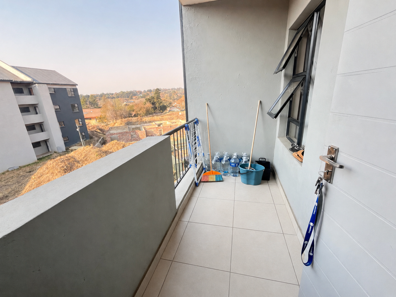A clean, tiled balcony area featuring a metal balustrade and views of the surrounding residential development.
