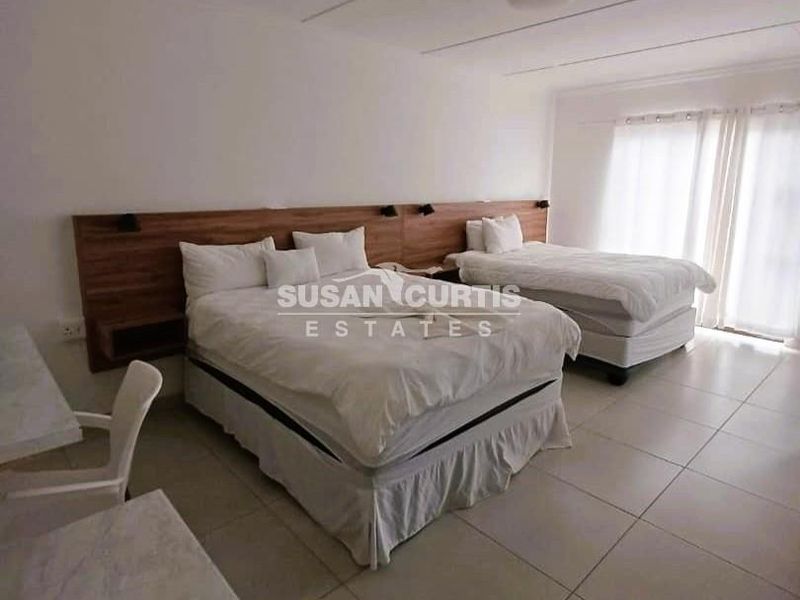 Spacious guest bedroom featuring a modern built-in wooden headboard, neutral tiled flooring, and direct access to the outdoors via sliding glass doors.