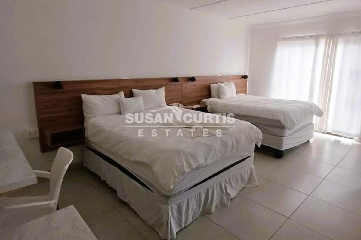 Spacious guest bedroom featuring a modern built-in wooden headboard, neutral tiled flooring, and direct access to the outdoors via sliding glass doors.