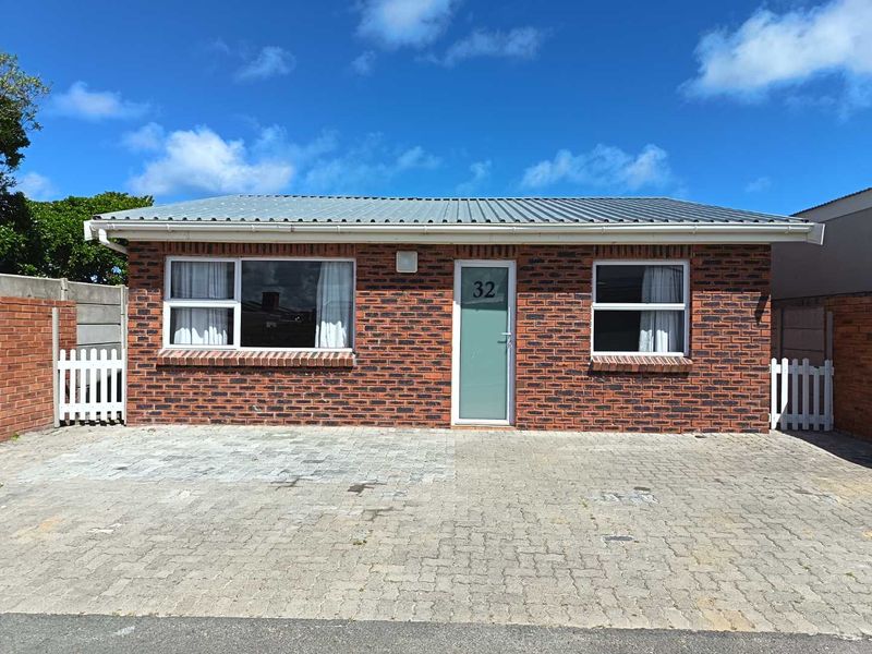 Front elevation of a single-story face brick house featuring a corrugated metal roof, paved driveway, and secure gated access.