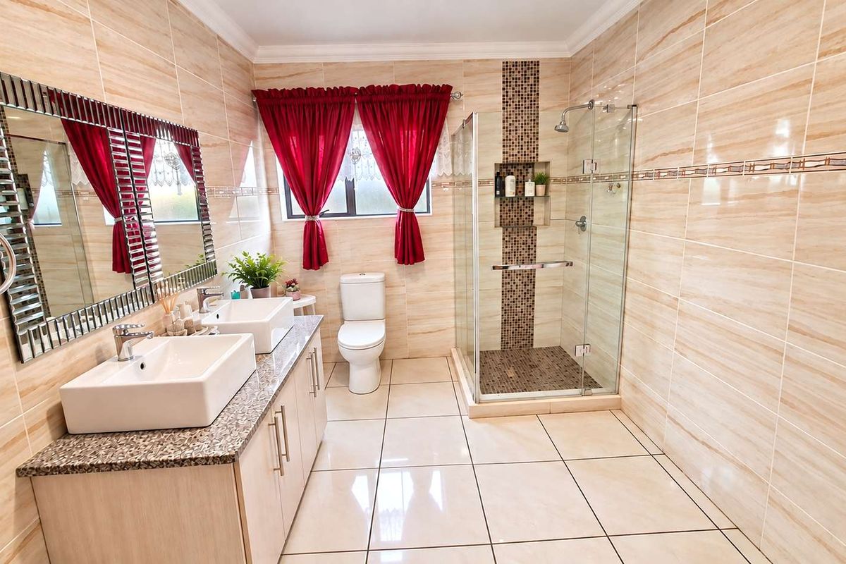 Modern bathroom featuring a double vanity with granite countertop, glass-enclosed shower with mosaic tile accents, and neutral ceramic wall and floor tiling.