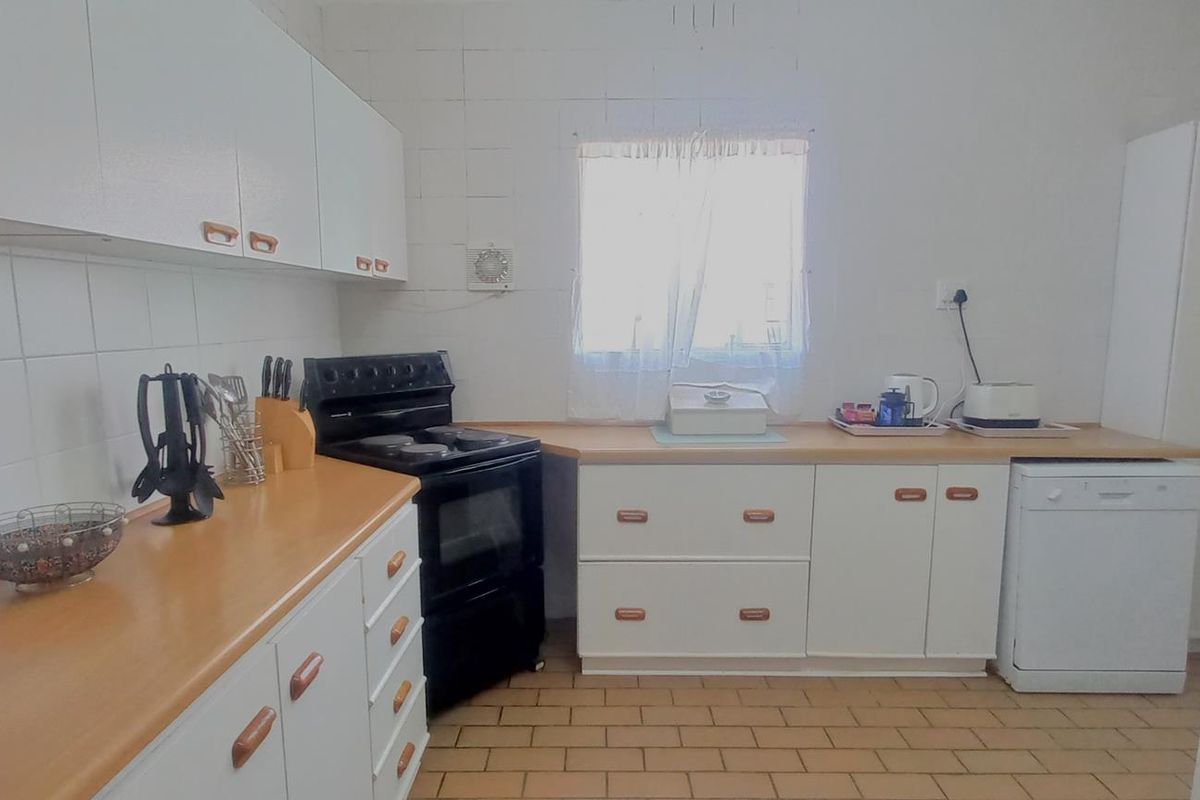 A functional kitchen featuring white cabinetry, laminate countertops, tiled backsplash, and a freestanding stove with tiled flooring.