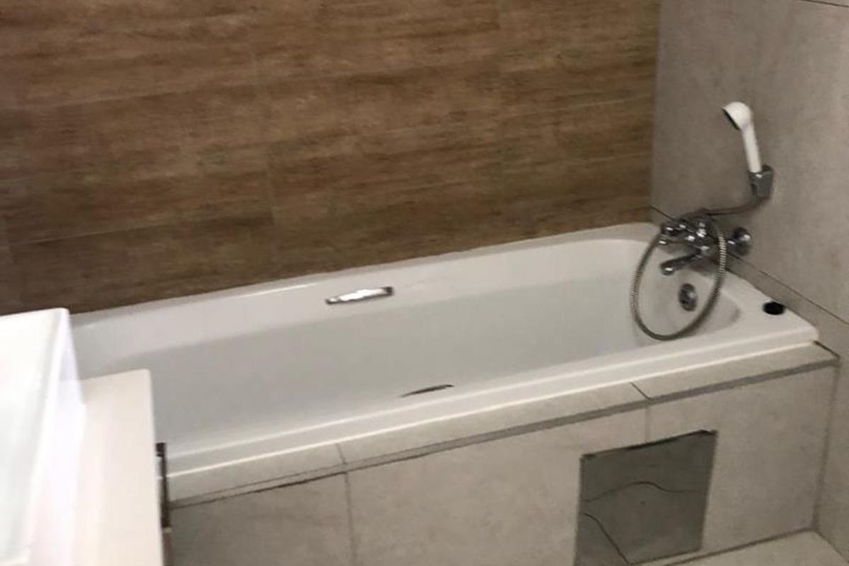A modern bathroom featuring a built-in bathtub with a handheld shower fixture, accented by wood-look wall tiling and neutral floor tiles.