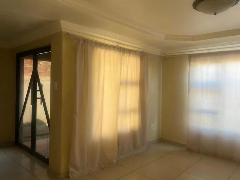 An empty living room featuring tiled flooring, ceiling cornices, and a sliding glass door providing access to the exterior.