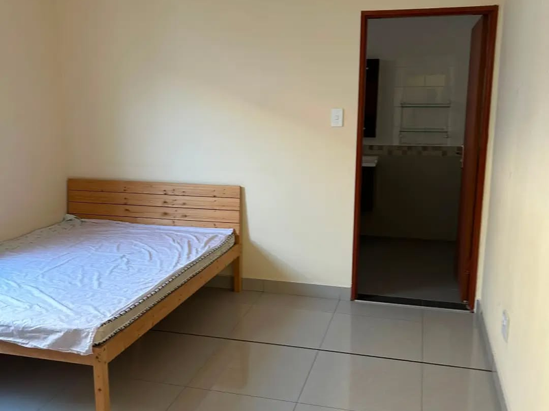 A simple bedroom featuring neutral walls and tiled flooring, with direct access to an adjoining bathroom.