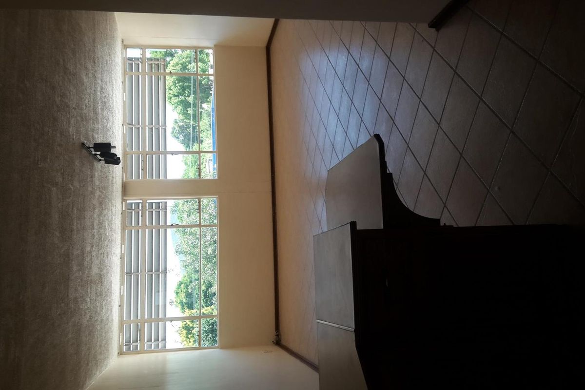 Spacious, empty living area featuring large windows, tiled and carpeted flooring, offering a bright and versatile space for potential interior design.