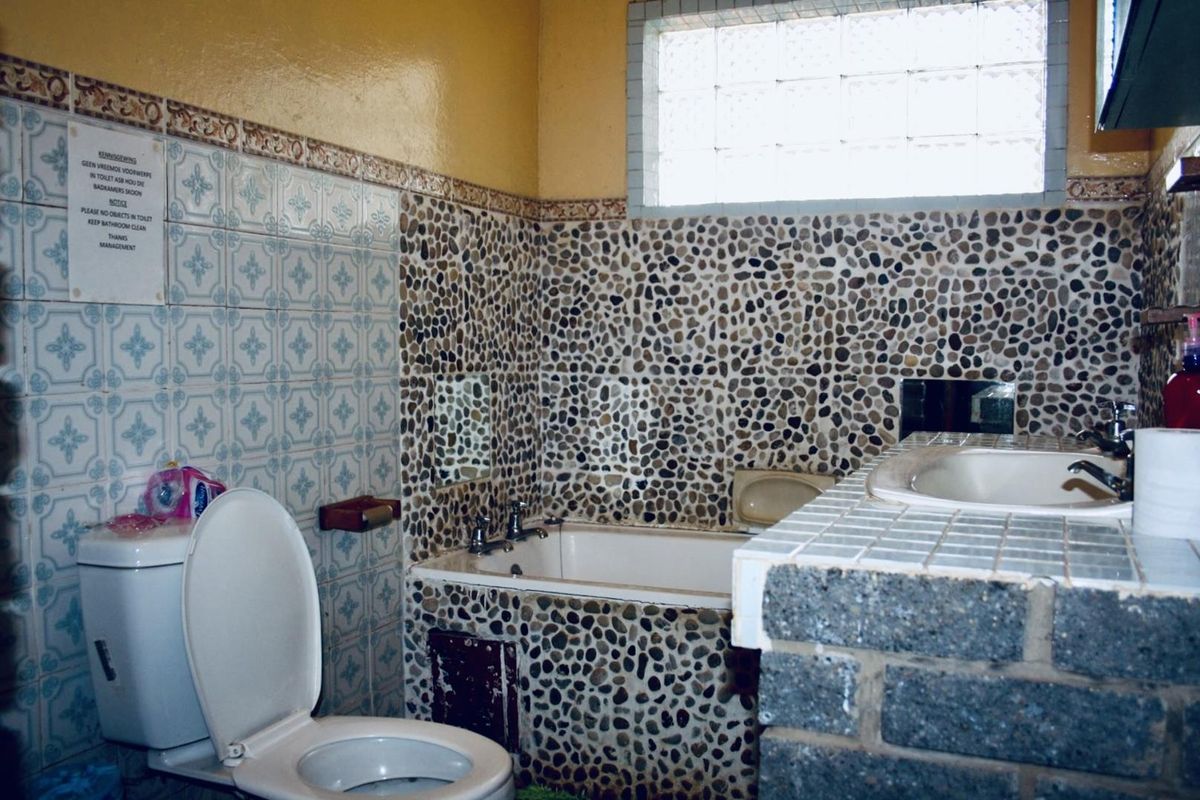 A dated bathroom featuring a built-in bathtub with pebble-tiled surround, a tiled vanity with integrated basin, and a glass block window.