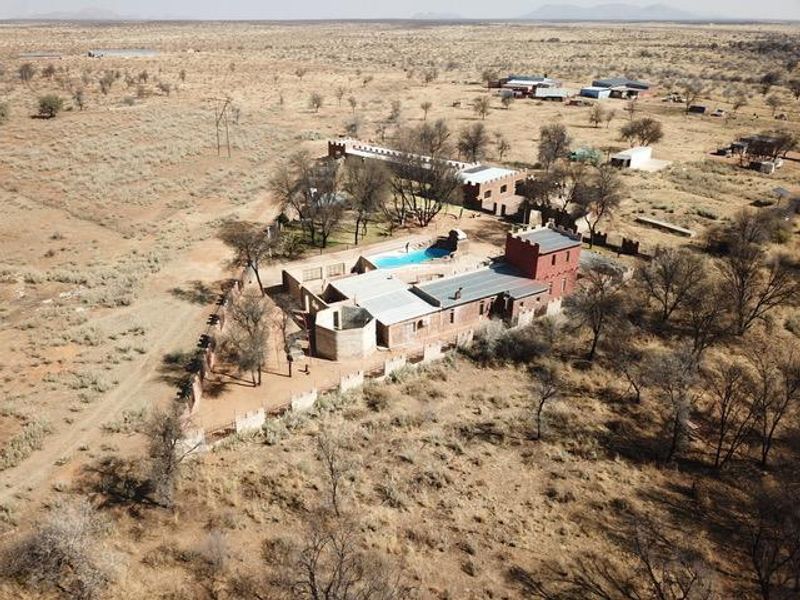 Aerial view of a small holding property featuring a main dwelling with turret architecture, a swimming pool, and surrounding arid landscape.