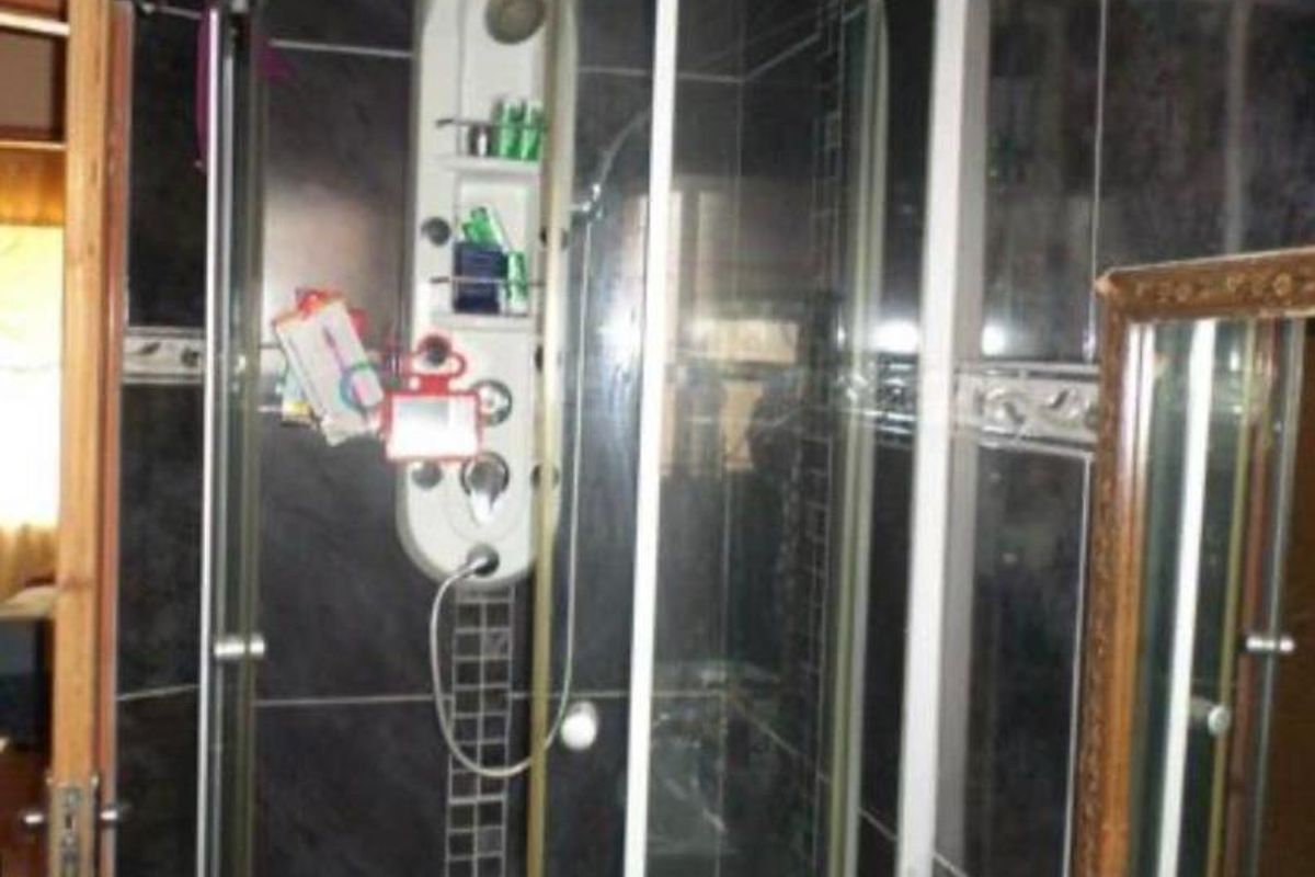 A bathroom featuring a corner shower enclosure with a built-in shower panel and dark wall tiling.