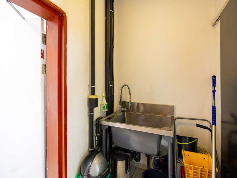 A functional utility space featuring a stainless steel sink and exposed plumbing, suitable for cleaning or maintenance tasks.