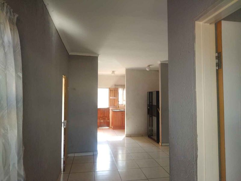 A view through a hallway with tiled flooring leading towards a kitchen area, featuring neutral wall tones and standard internal door frames.