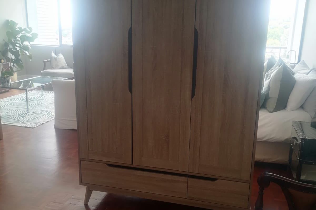 A bedroom featuring parquet flooring and large windows, currently occupied by a large wardrobe.