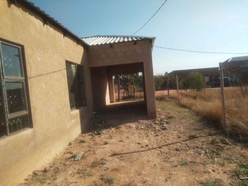 Rear view of the property showing an unfinished exterior wall, aluminium window frames, and a covered patio area leading to an unlandscaped yard.