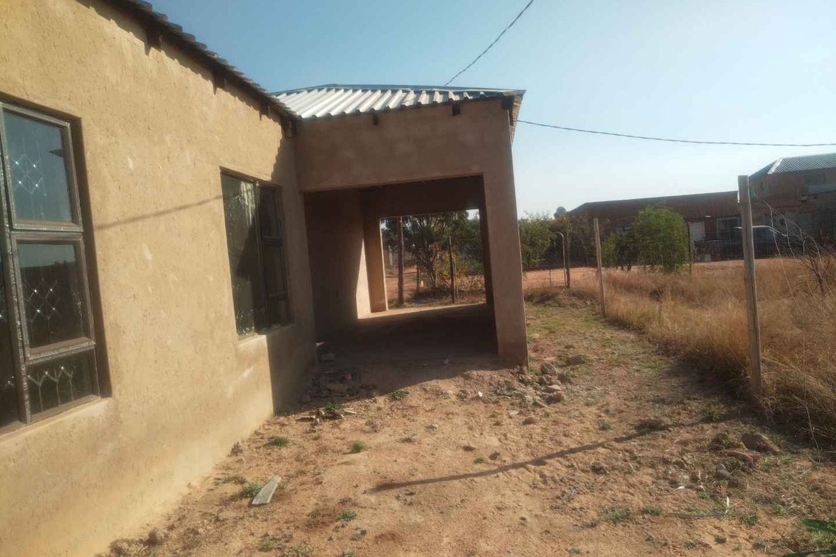Rear view of the property showing an unfinished exterior wall, aluminium window frames, and a covered patio area leading to an unlandscaped yard.